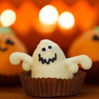 A cupcake styled in the shape of a googly-eyed ghost, with two smiling pumpkin-shaped cupcakes behind it.